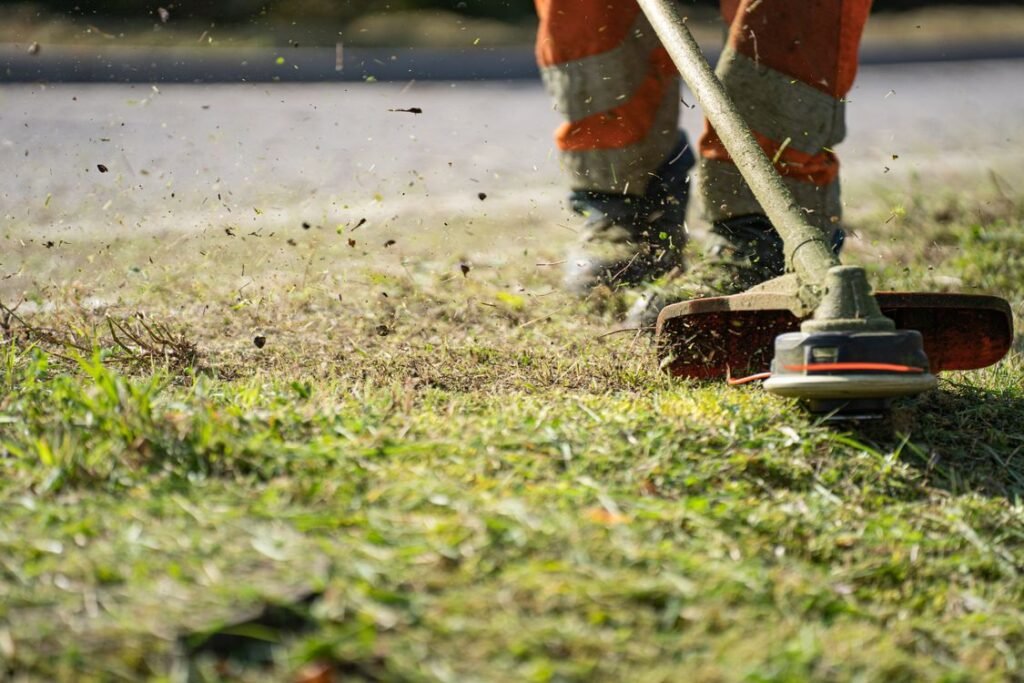 A worker trimming grass with a power tool at a customer site