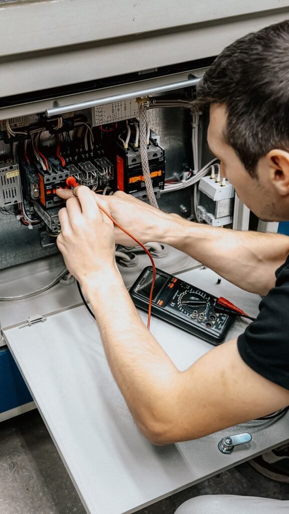 Electrician testing connections in an open electrical panel with a multimeter