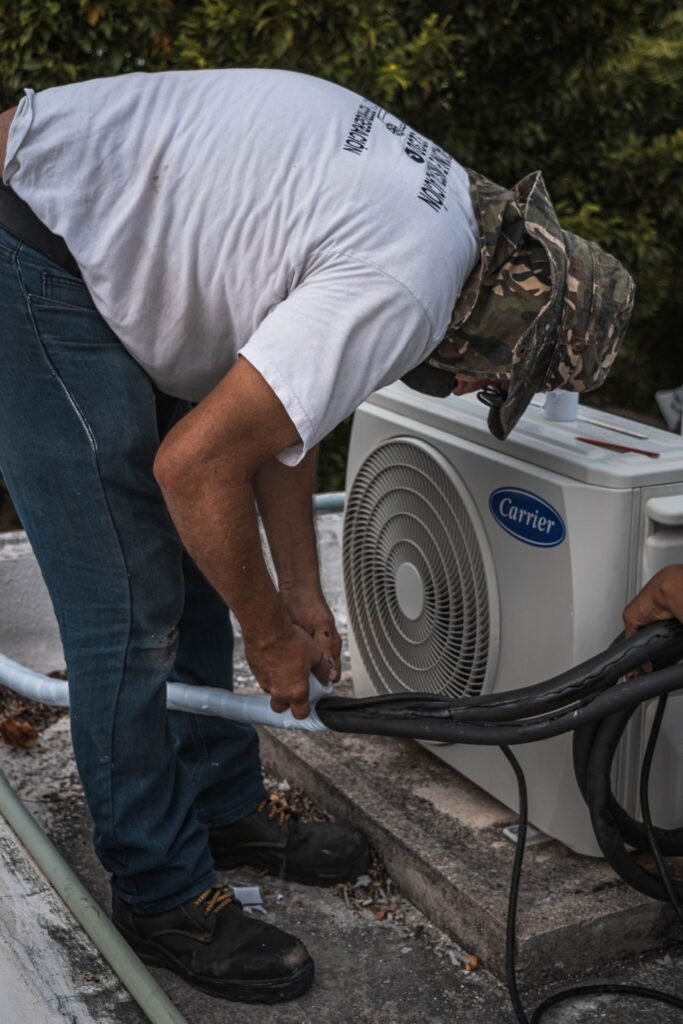 Technician taping refrigerant hose insulation beside a home air conditioning unit
