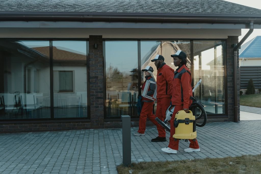 Professional cleaning team in uniforms with equipment approaching a house