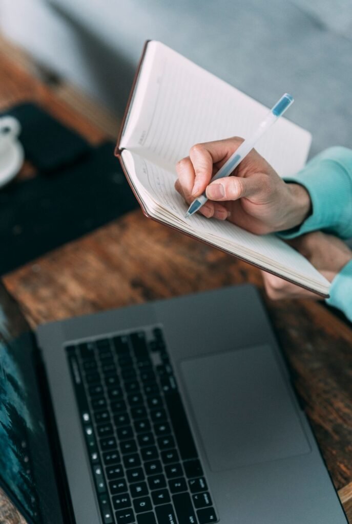 Person writing notes at a desk with a laptop