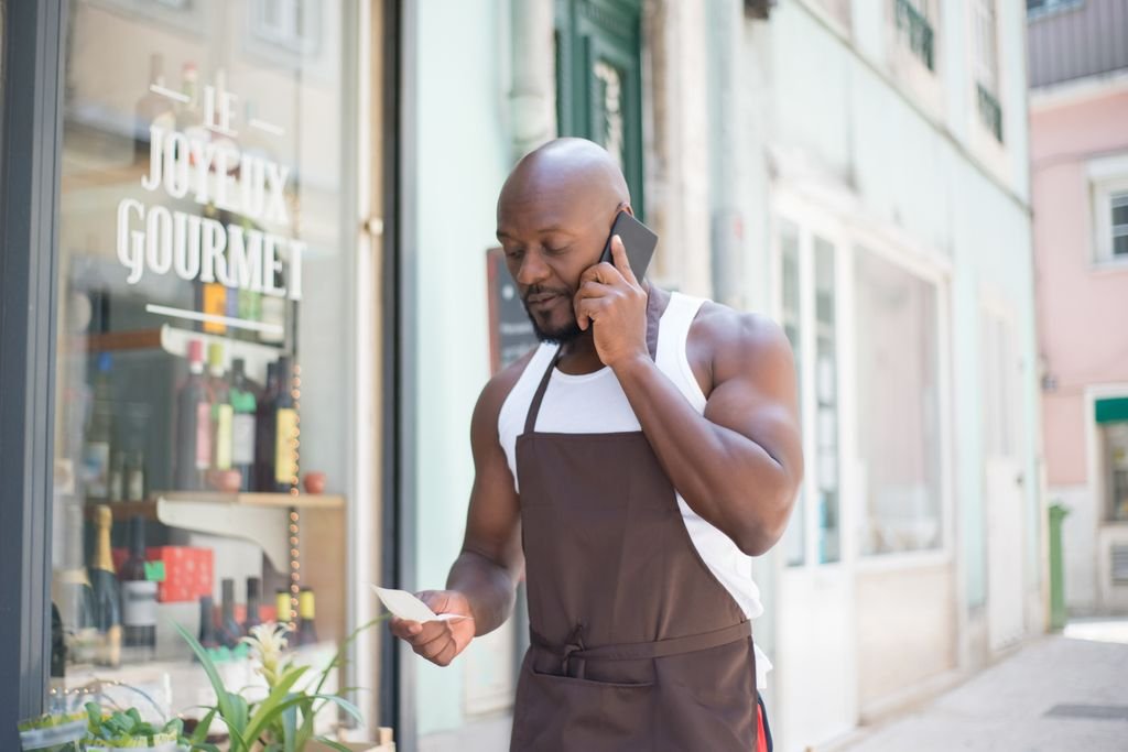 Small business owner in an apron making a business call outside a store
