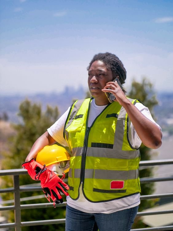 Construction worker in safety gear using a phone outdoors
