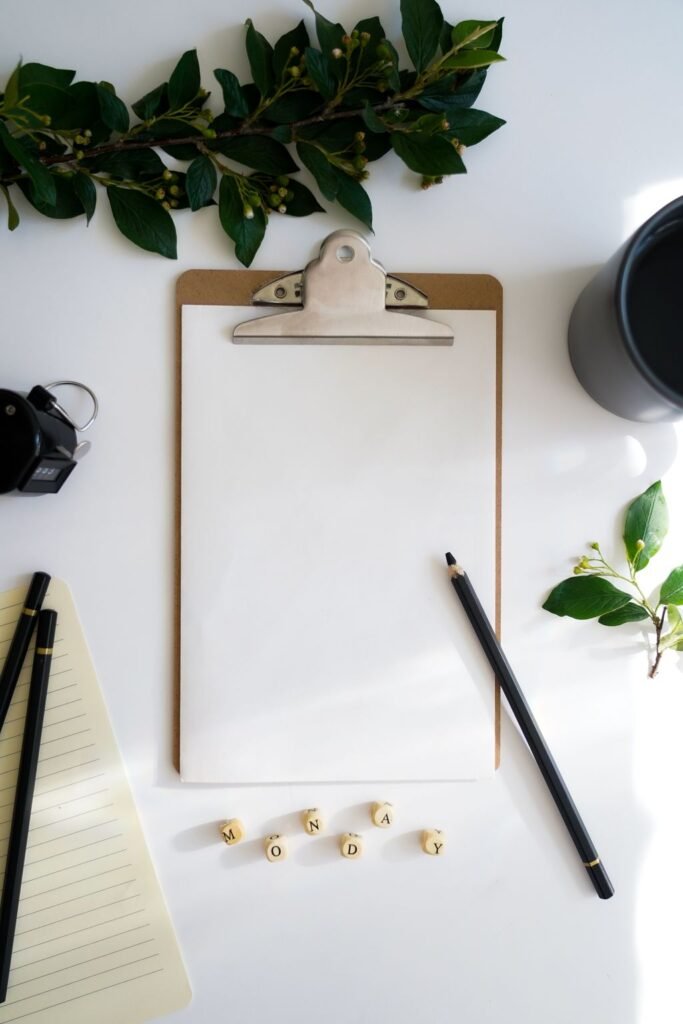 Flat lay of a clipboard, pencil, and greenery accents on a white desk