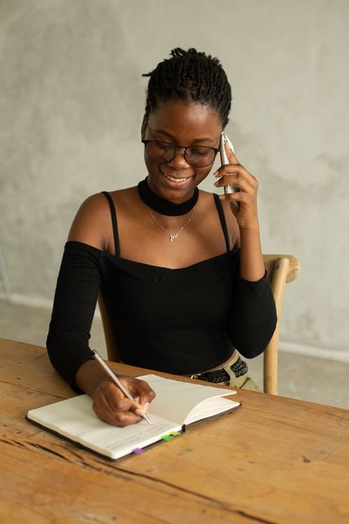 A woman writing notes in a notebook while talking on the phone